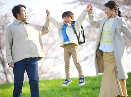 両親と手をつなぎよろこぶ小学生