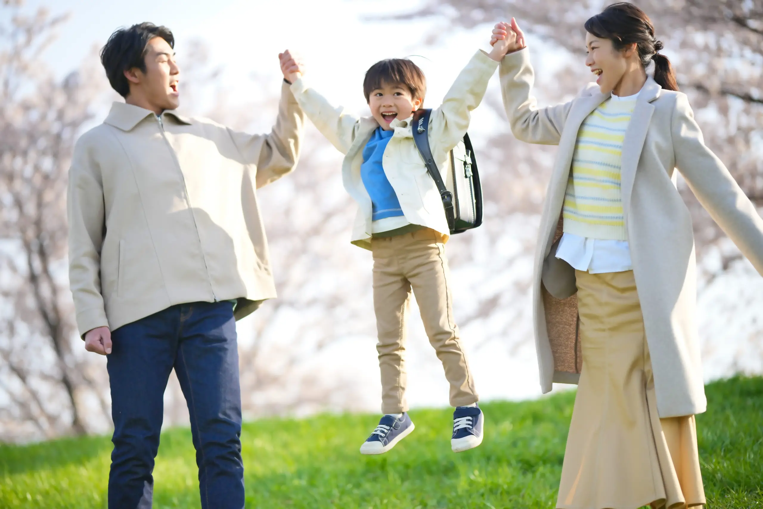 両親と手をつなぎよろこぶ小学生