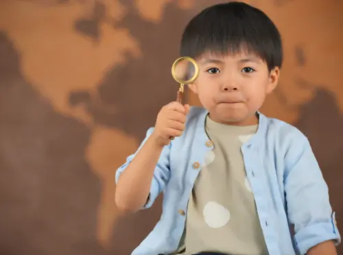 世界地図を背景に虫眼鏡を持つ男の子