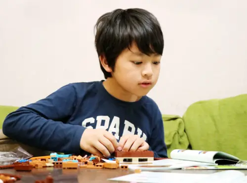 室内でおもちゃを組み立てながら一人で遊ぶ小学生