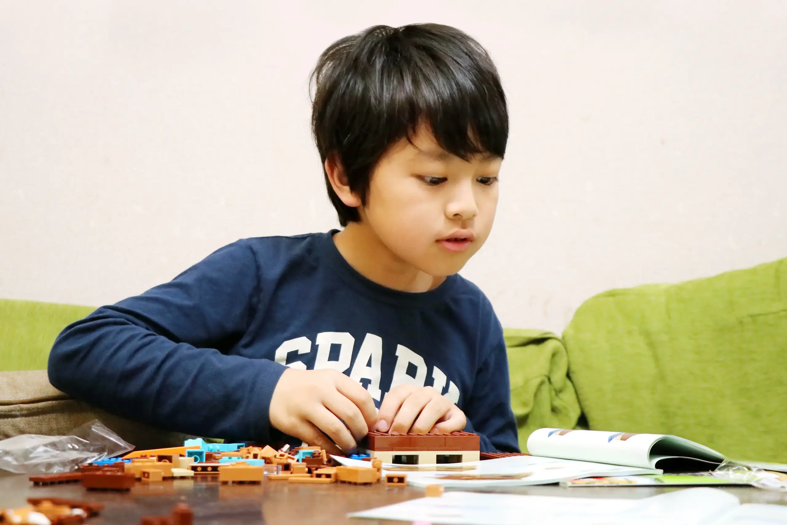室内でおもちゃを組み立てながら一人で遊ぶ小学生